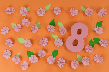 International Women Day. Pink origami flowers with paper green leaves, on orange background.