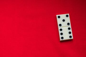 The game of dominoes. One domino bone lies on a red rag background and a lot of space for text