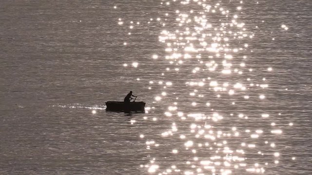 Un pescador navega a remo en un mar de estrellas producidas por el reflejo del sol en el agua