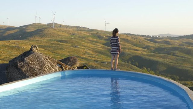 Woman in Casa do Penedo Boulder House swimming pool with view to wind turbines landscape in Fafe, Portugal
