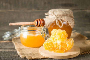 Honey dripping from a wooden honey dipper in a jar on wooden grey rustic background