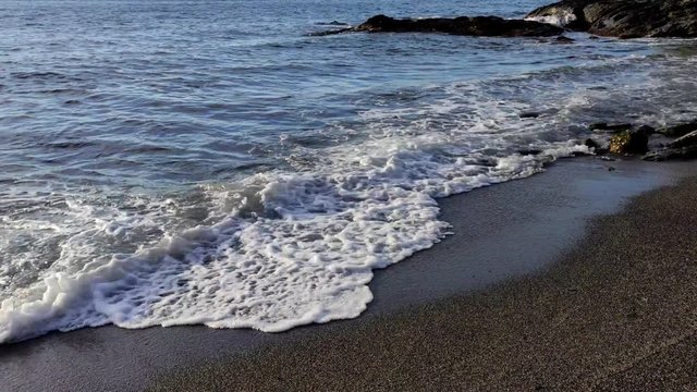Olas suaves rompen sobre la arena entre arrecifes y generan espuma marina