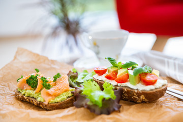 Wholegrain toast with avocado, tomato and salmon on wooden cutting board