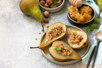 Healthy diet dessert. Baked pears with hazelnuts, honey and granola on a slate, stone or concrete background. Copy space.