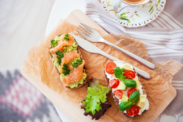 Wholegrain toast with avocado, tomato and salmon on wooden cutting board