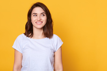 Close up portrait of attractive woman with dark hair being very glad, smiling with broad smile, showing her perfect teeth, looking aside, joyful excited cheery femlae. Copy space for advertisment.