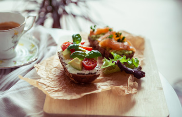 Wholegrain toast with avocado, tomato and salmon on wooden cutting board