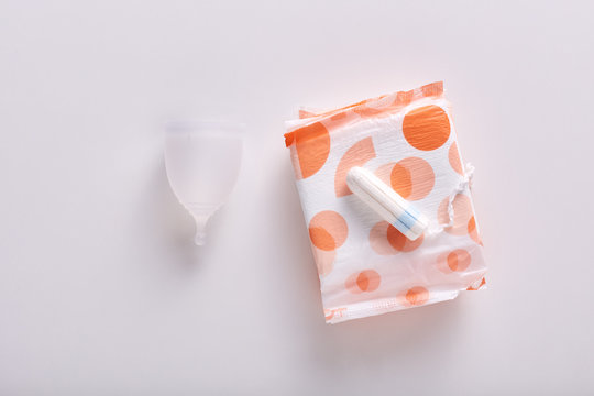 Horizontal flat lay of different types of feminine hygiene products for menstruation. Menstrual cup, packed sanitary pad and tampon laying on it, being isolated over white background. Periods concept.