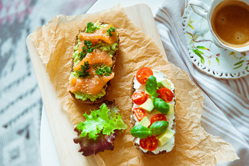 Wholegrain toast with avocado, tomato and salmon on wooden cutting board