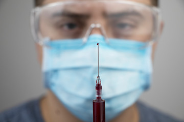 A male doctor looks at a syringe with blood. Blood sampling for analysis in the laboratory. Light...