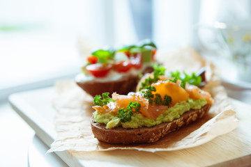 Wholegrain toast with avocado, tomato and salmon on wooden cutting board