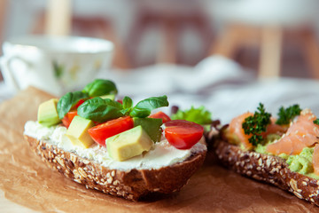 Wholegrain toast with avocado, tomato and salmon on wooden cutting board