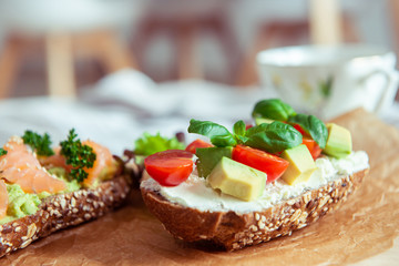 Wholegrain toast with avocado, tomato and salmon on wooden cutting board