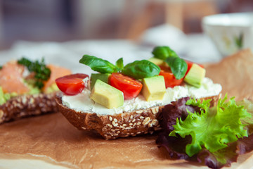 Wholegrain toast with avocado, tomato and salmon on wooden cutting board