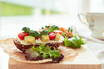 Wholegrain toast with avocado, tomato and salmon on wooden cutting board