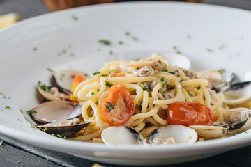 Pasta with clams on white plate on black background. Mediterranean delicacy food. Flat lay. Top view