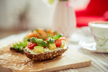 Wholegrain toast with avocado, tomato and salmon on wooden cutting board