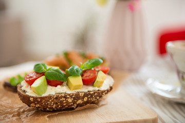 Wholegrain toast with avocado, tomato and salmon on wooden cutting board