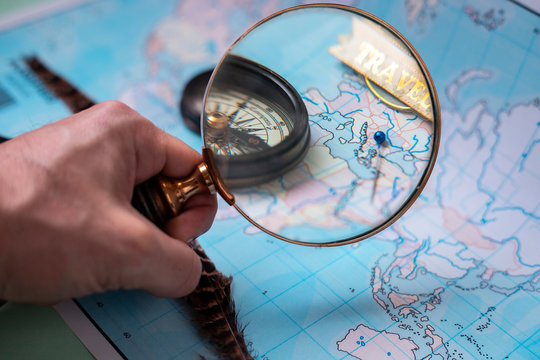  holding a magnifying glass with the hand focusing a compass and a pushpin on a map, travel concept