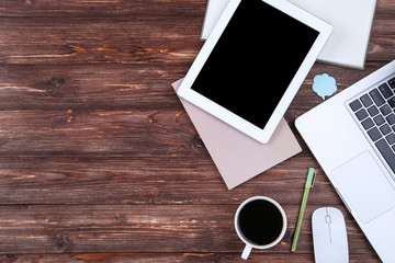 Laptop and tablet computer with notepads and cup of coffee on wooden table