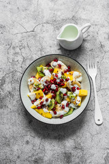 Coconut yogurt and tropical fruit salad for breakfast, snack, dessert. Salad with greek yogurt, banana, mango, kiwi, pomegranate seeds and flaxseeds on a gray background. the view from the top