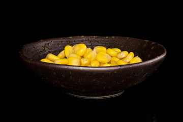 Lot of pieces of canned yellow corn in glazed bowl isolated on black glass