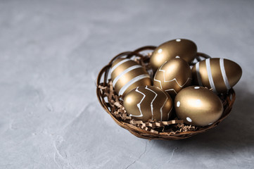 Easter decorative eggs in gold color with a pattern in a basket on a gray background