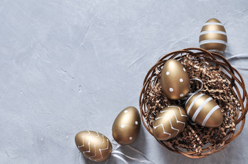Easter decorative eggs in gold color with a pattern in a basket on a gray background