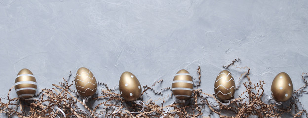 Decorative Easter eggs in gold color with a pattern and paper decor on a gray background