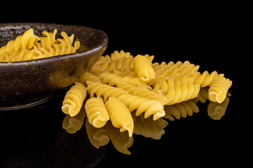 Lot of whole yellow pasta fusilli in glazed bowl isolated on black glass