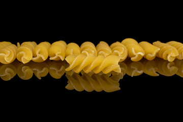 Lot of whole yellow pasta fusilli isolated on black glass