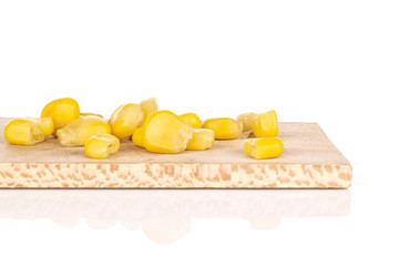 Lot of pieces of canned yellow corn on wooden cutting board isolated on white background