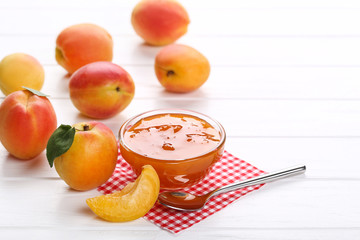 Jam in bowl and apricots on white wooden table