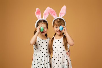happy cute little child girls with pink bunny ears holding painted Easter eggs on studio yellow background. Easter day