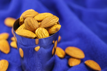 Almonds in a metal glass and on a blue background