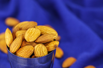 Almonds in a metal glass on a blurry blue background