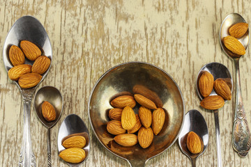 Metal spoons with almonds on a light wooden surface