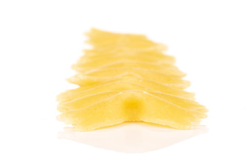 Lot of whole yellow pasta farfalle in row isolated on white background