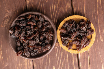 Lot of whole dried dark raisin on round bamboo coaster with brown ceramic coaster flatlay on brown wood