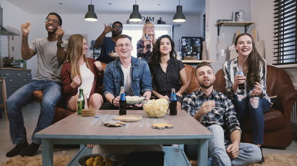 Diverse group of friends watching sports on TV Football supporters celebrate success with popcorn...