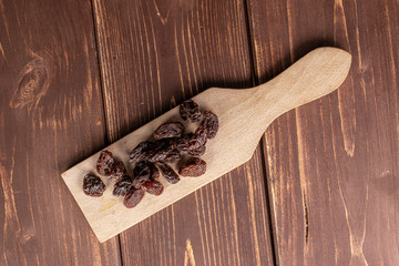 Lot of whole dried dark raisin on wooden cutting board flatlay on brown wood