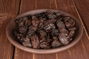 Lot of whole dried dark raisin with brown ceramic coaster on brown wood