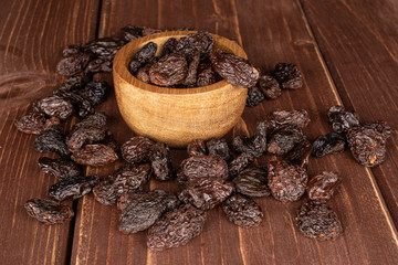 Lot of whole dried dark raisin in bamboo bowl on brown wood