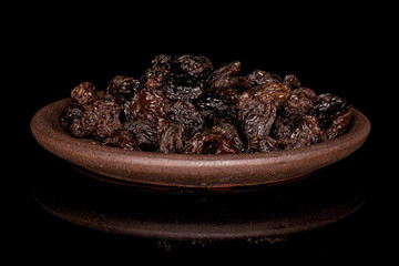 Lot of whole dried dark raisin with brown ceramic coaster isolated on black glass