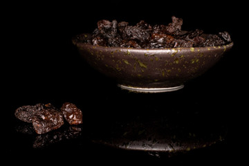 Lot of whole sweet dried dark raisin in glazed bowl isolated on black glass