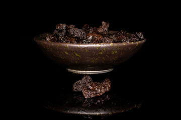 Lot of whole dried dark raisin in glazed bowl isolated on black glass