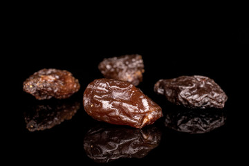 Group of four whole sweet dried dark raisin isolated on black glass