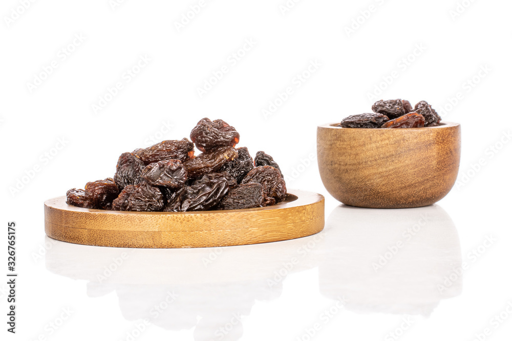 Wall mural Lot of whole dried dark raisin on round bamboo coaster in bamboo bowl isolated on white background