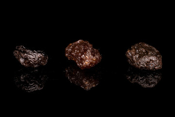 Group of three whole dried dark raisin isolated on black glass