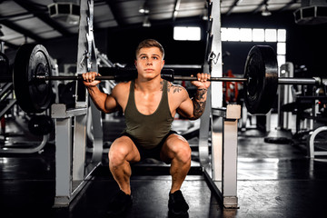 Fototapeta na wymiar Fit young man do squats with weights at the gym